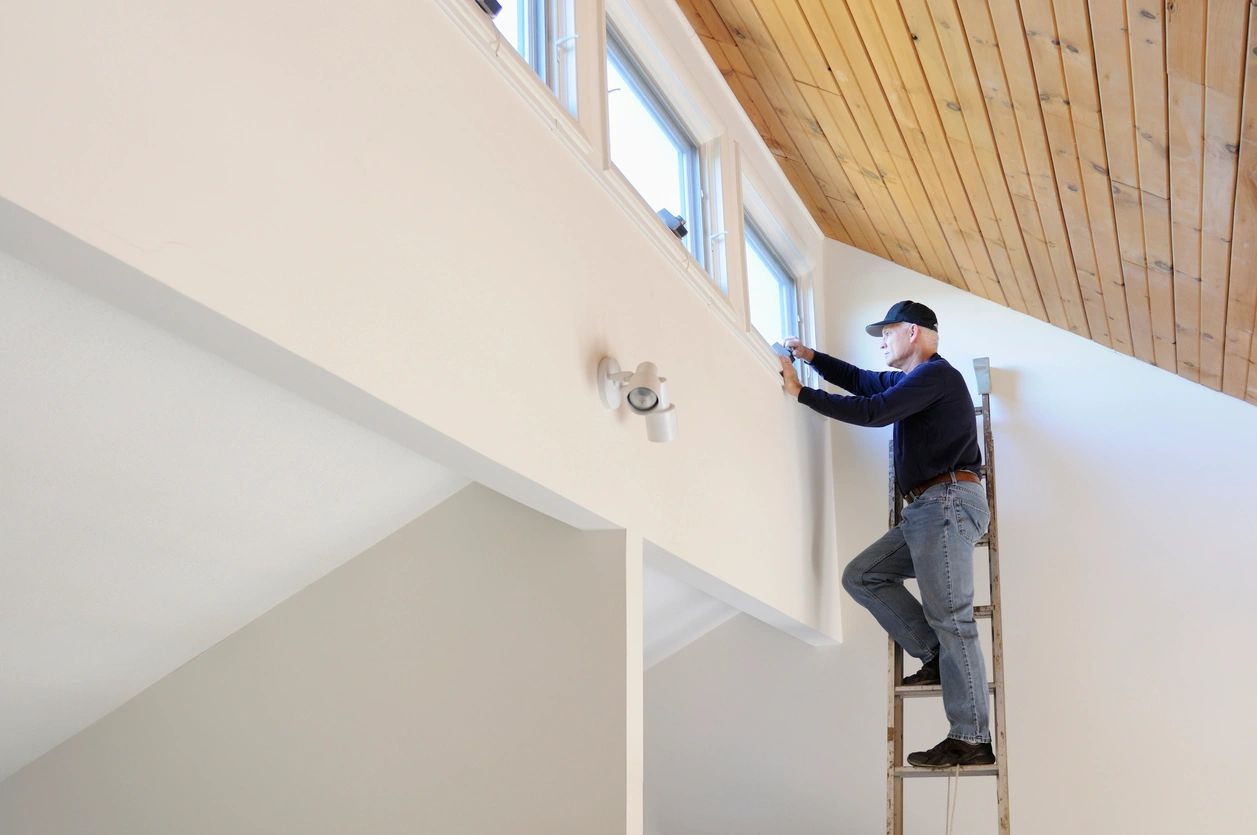 A man on a ladder painting the ceiling of a room.